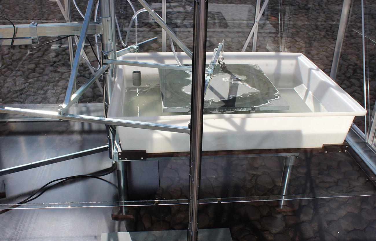 Afrundingsanordning (detail), 2015, The machine drips a circle of citric acid on a grey green lime stone (an exclusive lime stone in high quality, 60x60x2). The acid gradually dissolves a trace in the stone's surface, which over time rounds off the initially squared stone. Viborg Kunsthal.