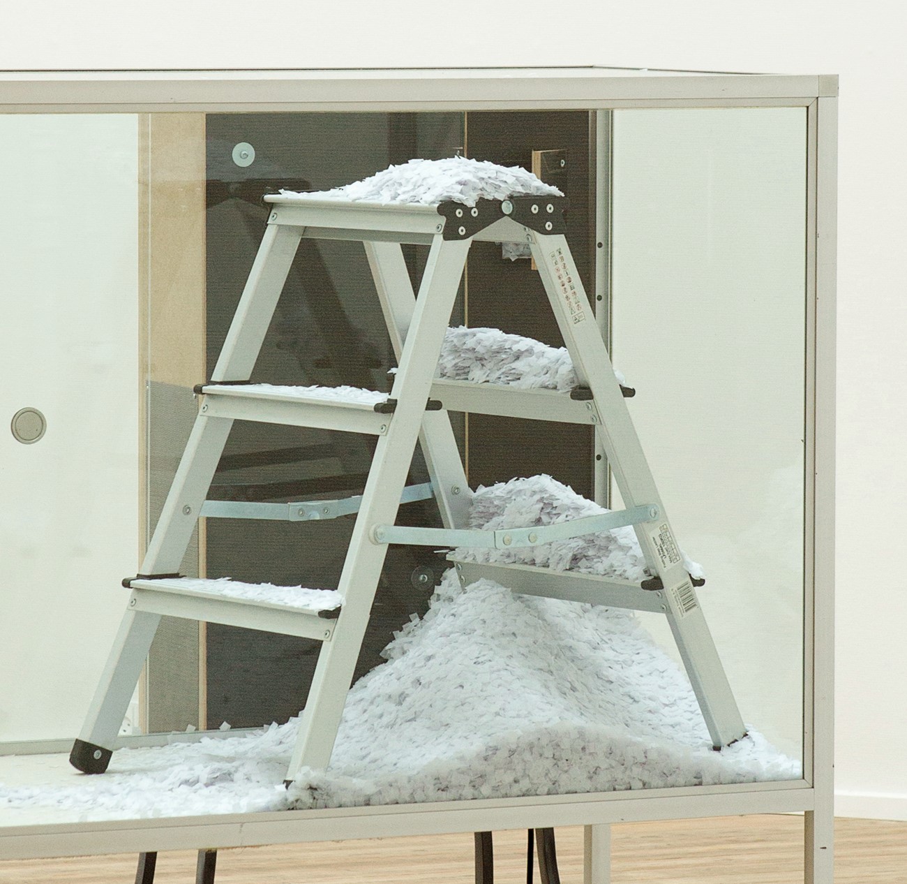 Konfetti 1, 2014, Fan, plywood, chipboard, MDF, iron and confetti, , 200x165x200 cm. , A machine blowing out confetti from a small hole at a very slow speed, a couple of confettis every 5th second. Kunsthal Aarhus.