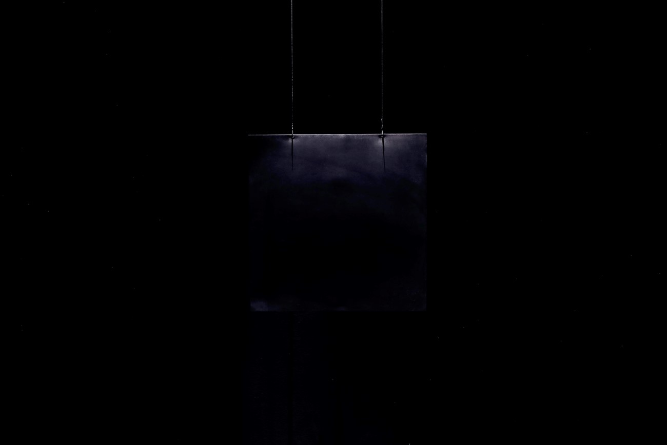 Black Metal Square — Black Metal Square, 2015, Black metal plate, sensor, contact speaker, light, amplifier and steel wire, 100 x 100 x 0.1 cm. Edition of 6 + 1 AP, Black Metal Square consists of a freely hanging black metal plate (100 x 100 x 0.1 cm). Its natural vibrations are enhanced and reflected back onto the plate in a constant replay. This type of subtle energy reflection reveals the resonance of the metal plate both visually as well as sonically. In 2015, Kirkegaard created Black Metal Square # 1 with inspiration from Kazimir Malevich’s painting Black Square from 1915 and the astronomer Robert Fludd’s drawing of a black square from 1617-21 with the text ‘Et sic in infinitum’ (And thus in all eternity).