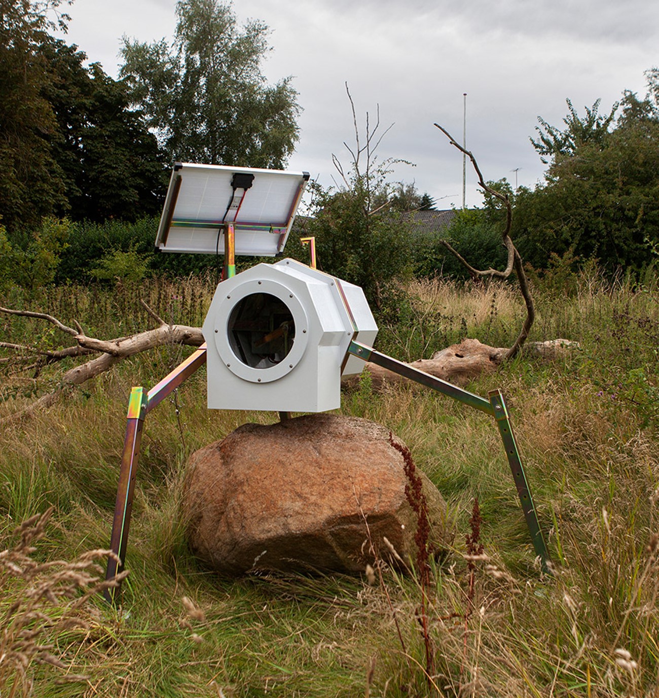 Markeringsapparatur, 2015, Wood, iron and electronics , 170 x 200 x 170 cm, The machine consists of a metal arm, circulating over the rock. On the arm is mounted a chisel, hitting the rock. The machine gets electricity from a solar cell and thereby depends on the amount of sunshine. On a sunny day in summertime, the amount of hits is every 5th minute, and in wintertime maybe one hit an hour. Over time will it make a groove in the rock. Sculpture village Selde.