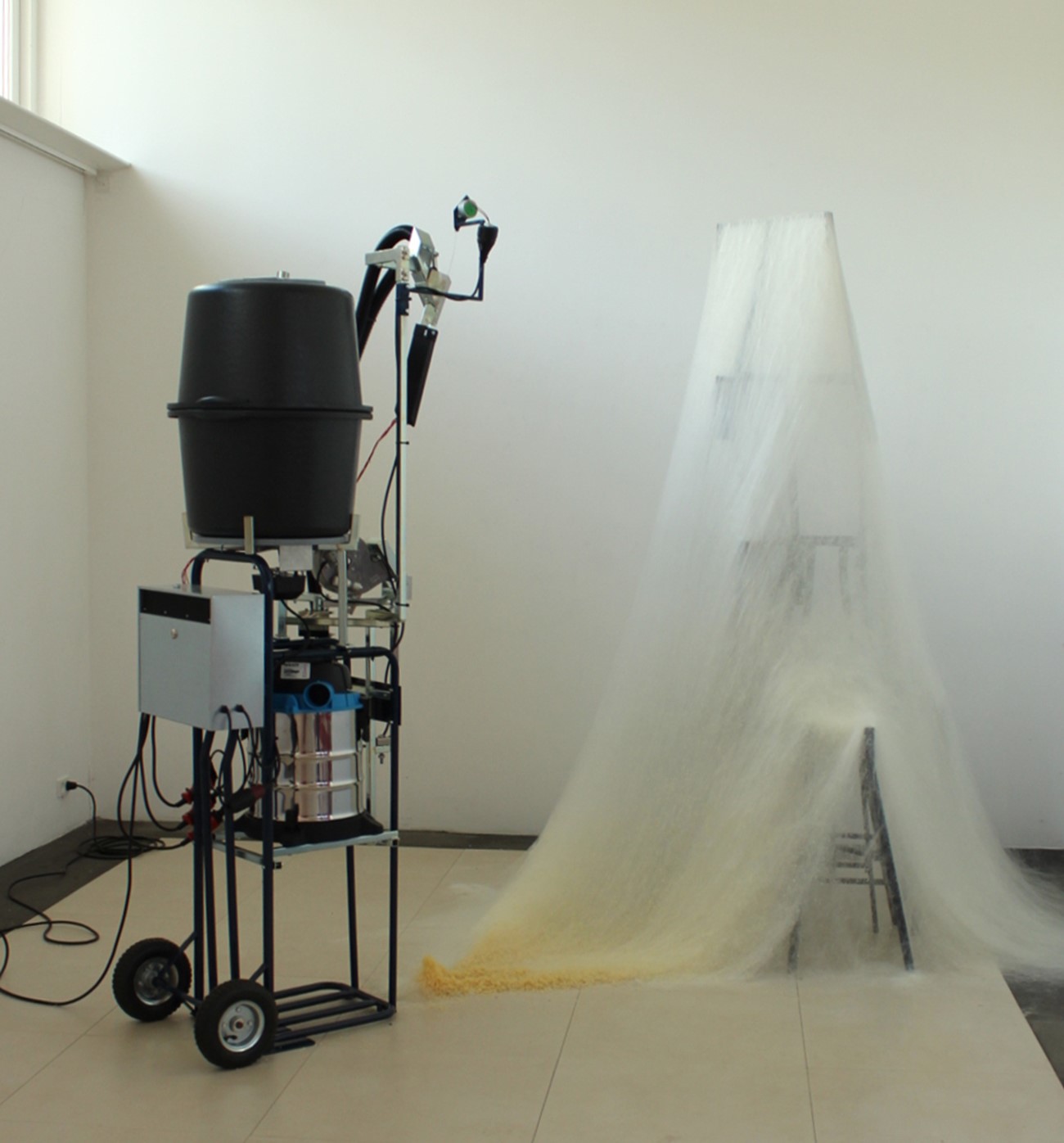 Multi Power L90, 2017, Glue, ventilator, iron, heat element, electronics and motor, 200 x 60 x 60 cm, The machine produces a white tissue of glue. The glue is heated in a small container and runs in thin threads down in front of the ventilator which blows the threads in different directions. Hereby, a white tissue is formed created which settles on the objects it comes across. Exhibited at Gammelgård, Herlev 2017.